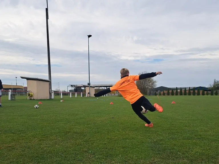 Junge im orangen Coerver-Trikot schießt den Ball volley